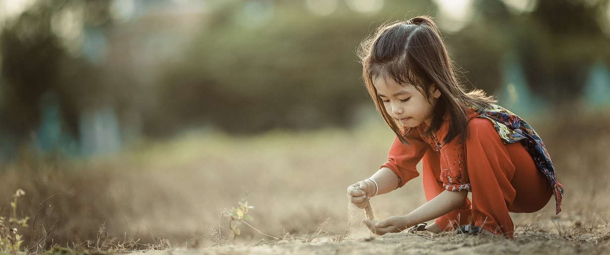 Encourage kids to closely examine Mother Earth to engage their tactile senses and natural curiosity. A young child sifts through the dirt.