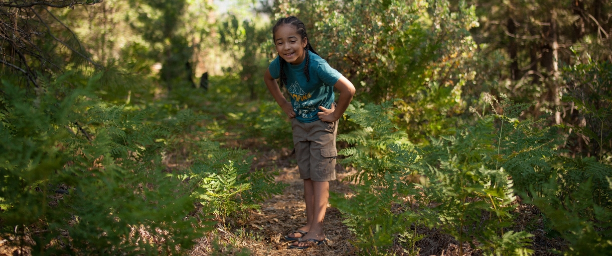 As you and your child happily explore the woods this Earth Day, tune into the beautiful sounds that nature has to offer. Child smiling while exploring the woods.